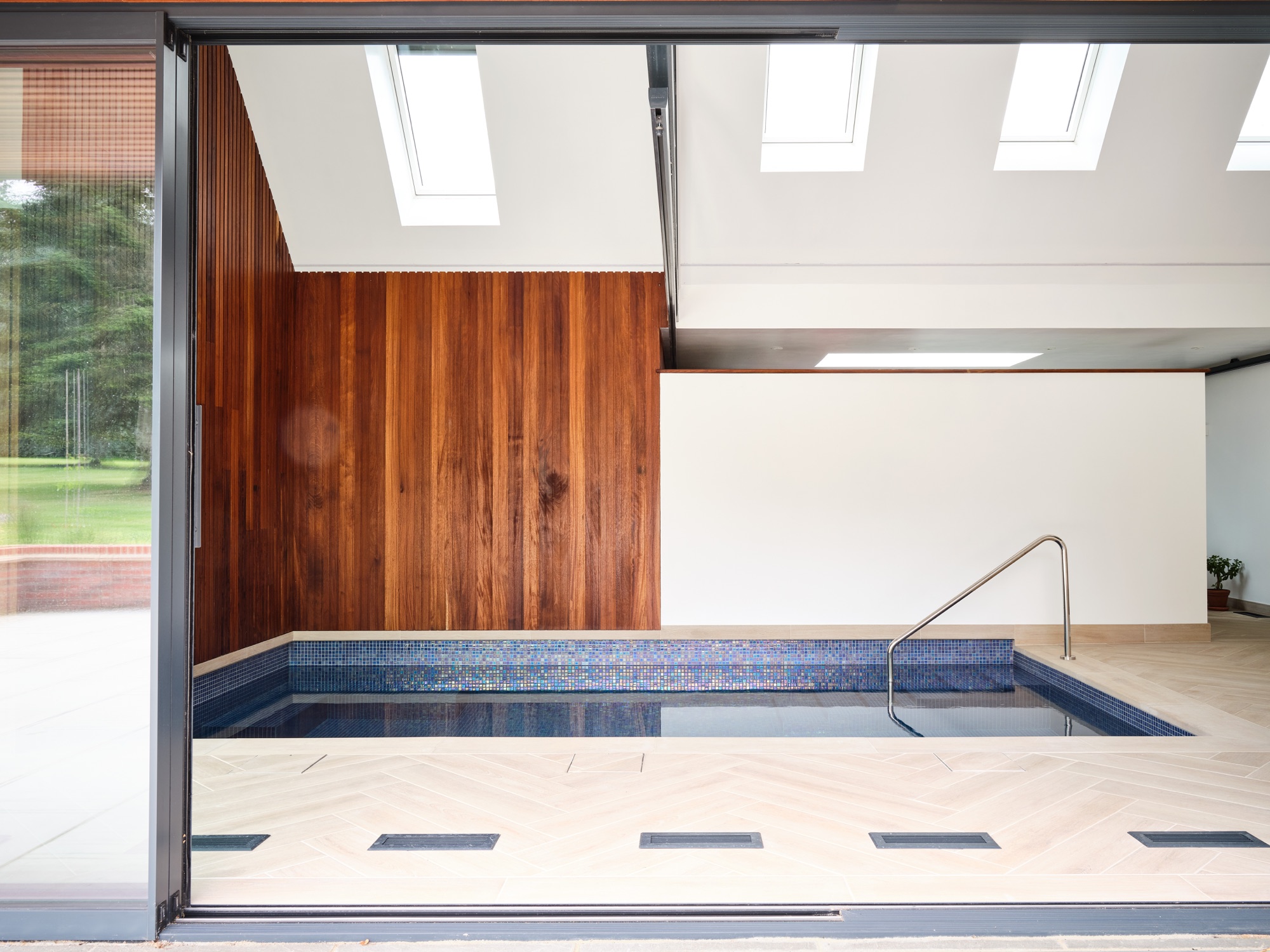 The Old Bakehouse pool extension &mdash; timber-clad gable, standing-seam zinc roof, warm Iroko soffit, and full-height glazing onto the terrace
