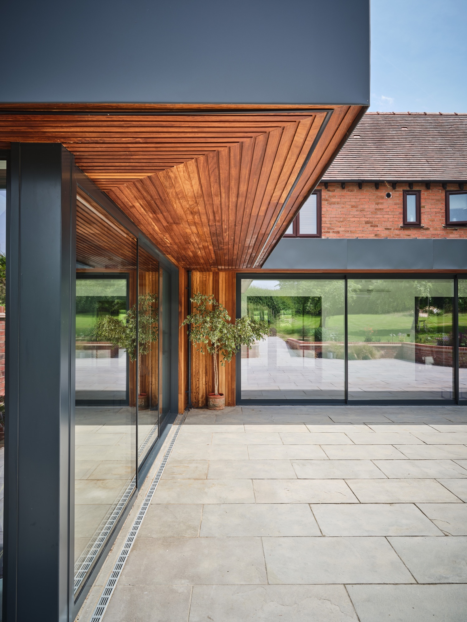Iroko soffit wrapping the corner of the extension &mdash; the terrace and full-height glazing beyond, countryside in the distance