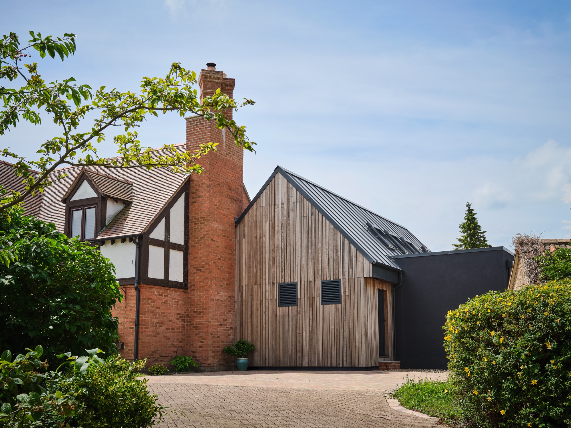 Approach view &mdash; the original red brick house and new timber-clad extension in counterpoint