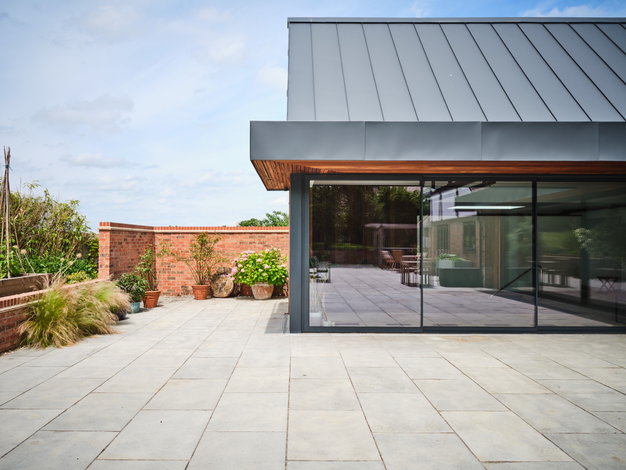 The terrace from the far end &mdash; zinc roof, full-height glazing, the pool visible inside
