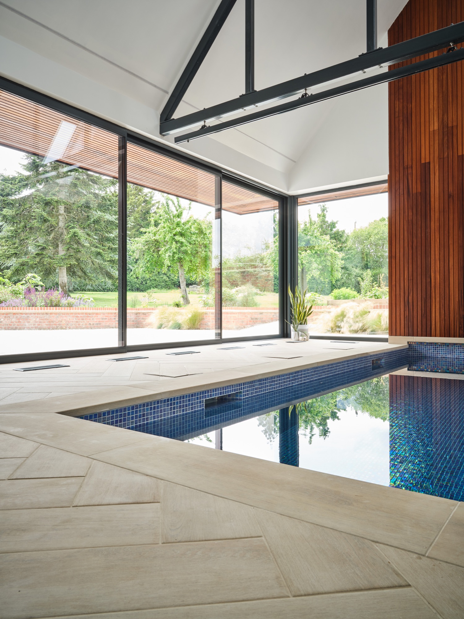The pool interior wide &mdash; full-length pool, herringbone limestone surround, and full-height glazing open to the garden